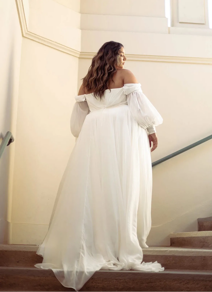 Woman in a white off-shoulder dress standing on a staircase