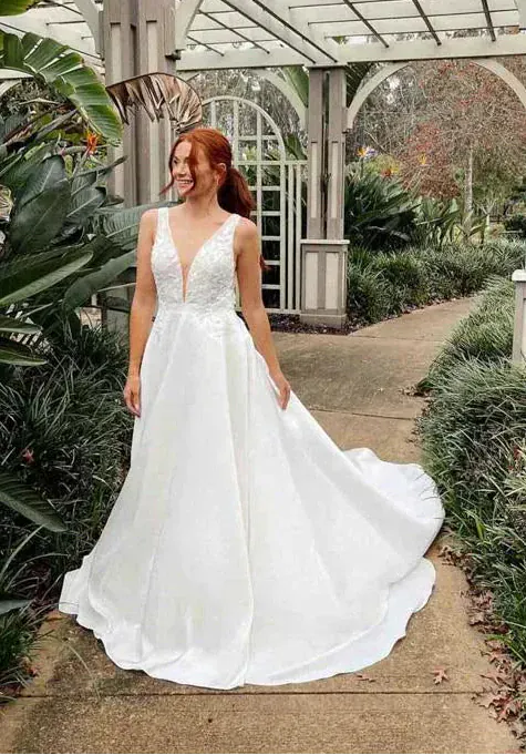 Woman in a white wedding dress standing outdoors with greenery and a gazebo in the background