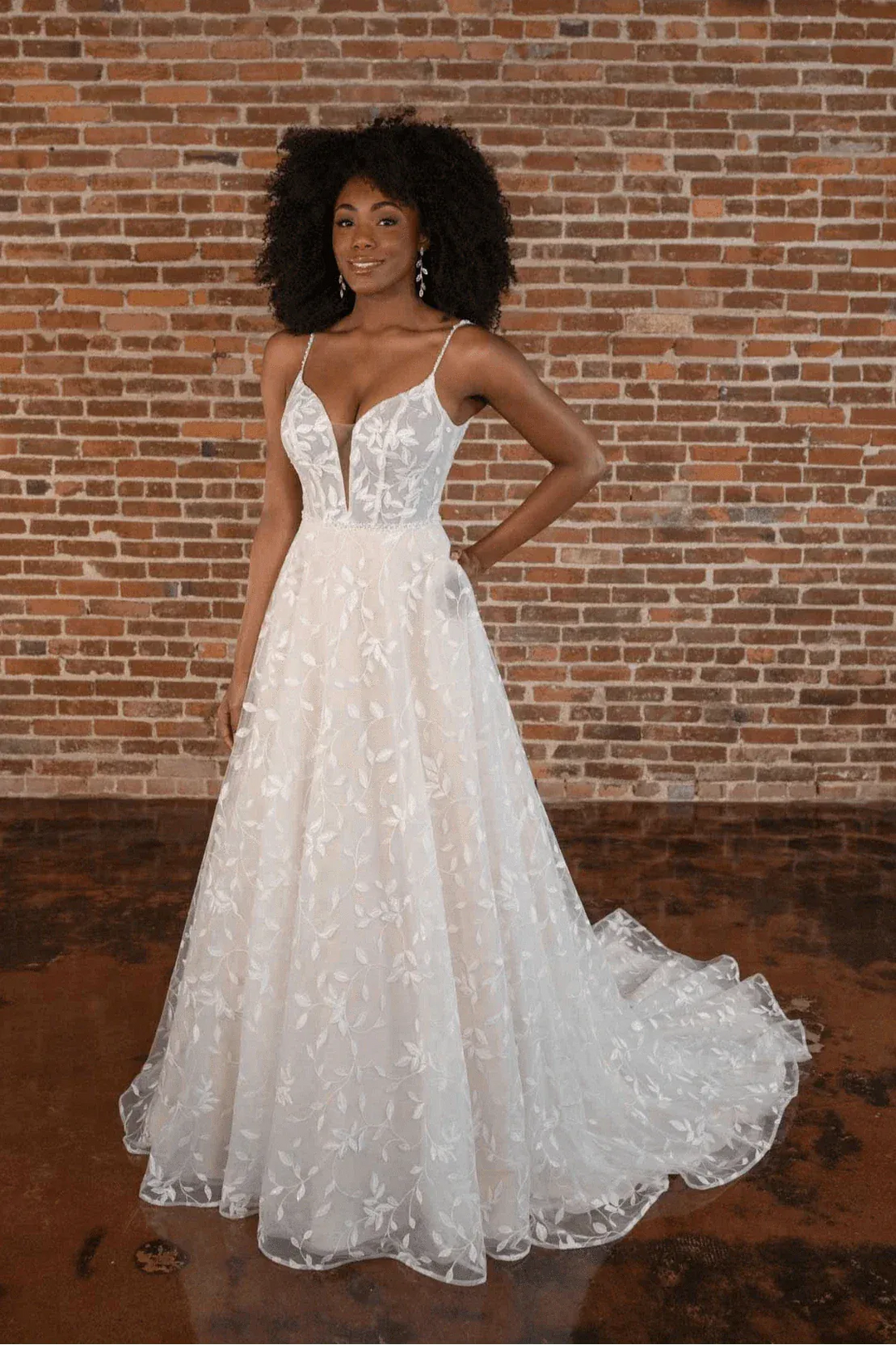 Woman wearing a white lace wedding dress against a brick wall.
