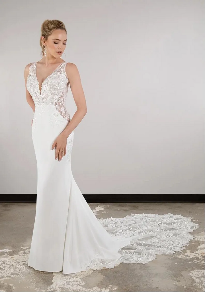 Woman wearing a white wedding dress with lace details on a plain background