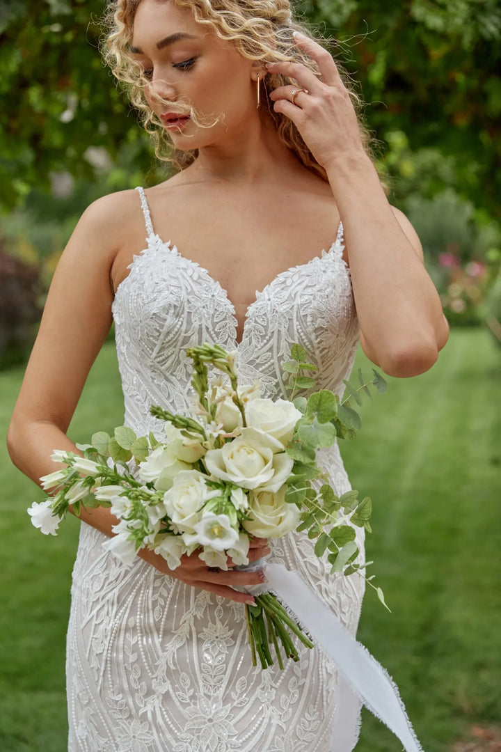 Woman in a white wedding dress holding a bouquet of flowers outdoors.