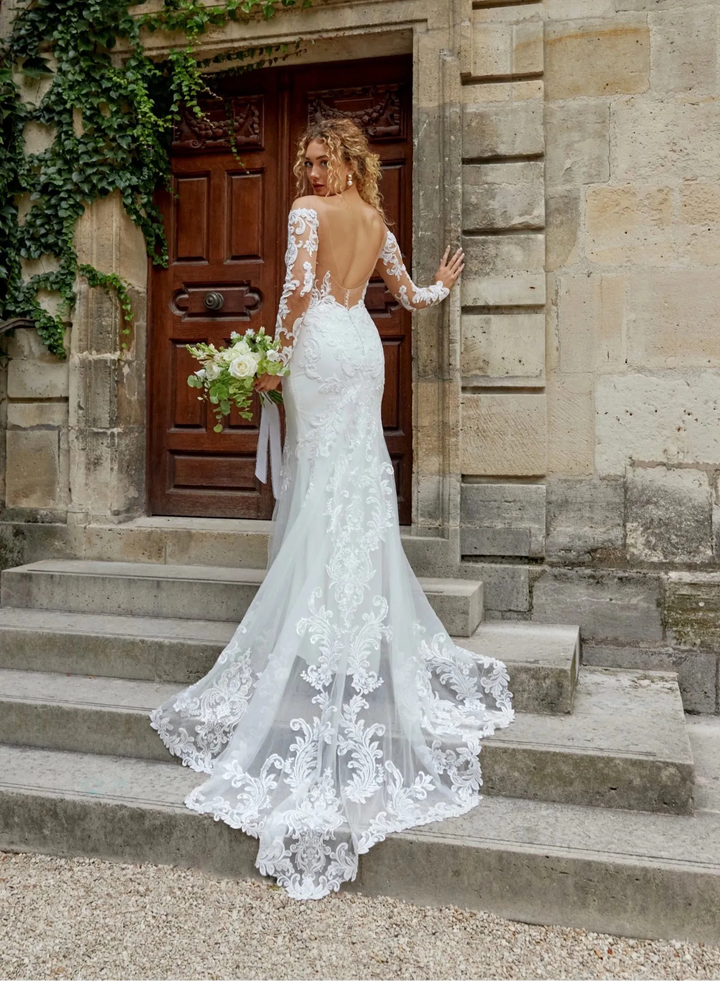 Bride in a white lace wedding dress standing on stone steps in front of an old building with ivy.