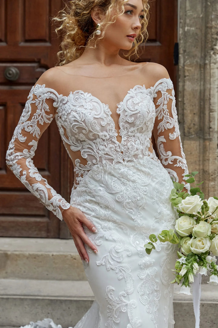 Woman in a white lace wedding dress holding flowers on steps.