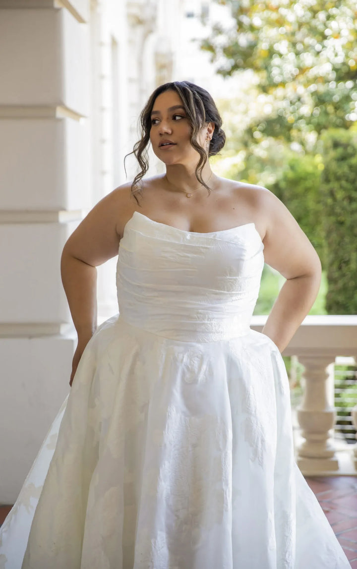 Woman wearing a white wedding dress standing outdoors with greenery in the background