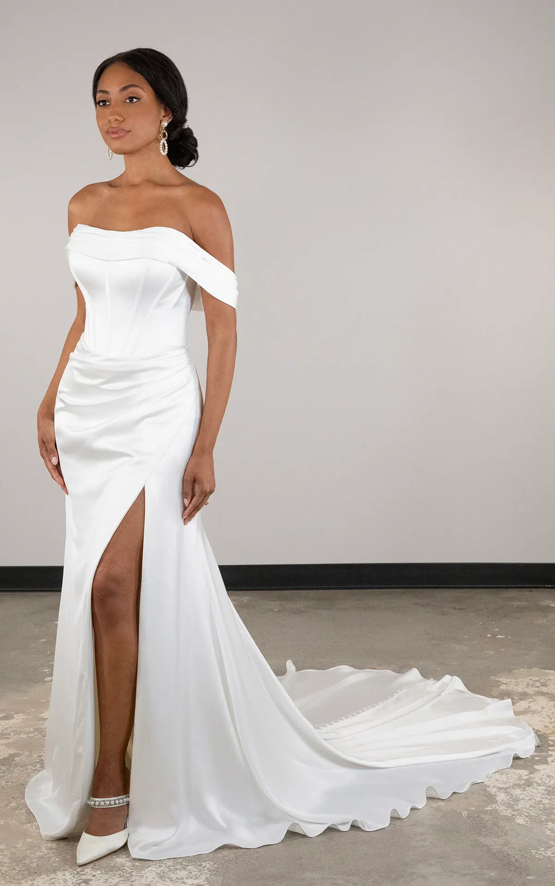 Woman wearing a white off-shoulder gown with a high slit on a plain background