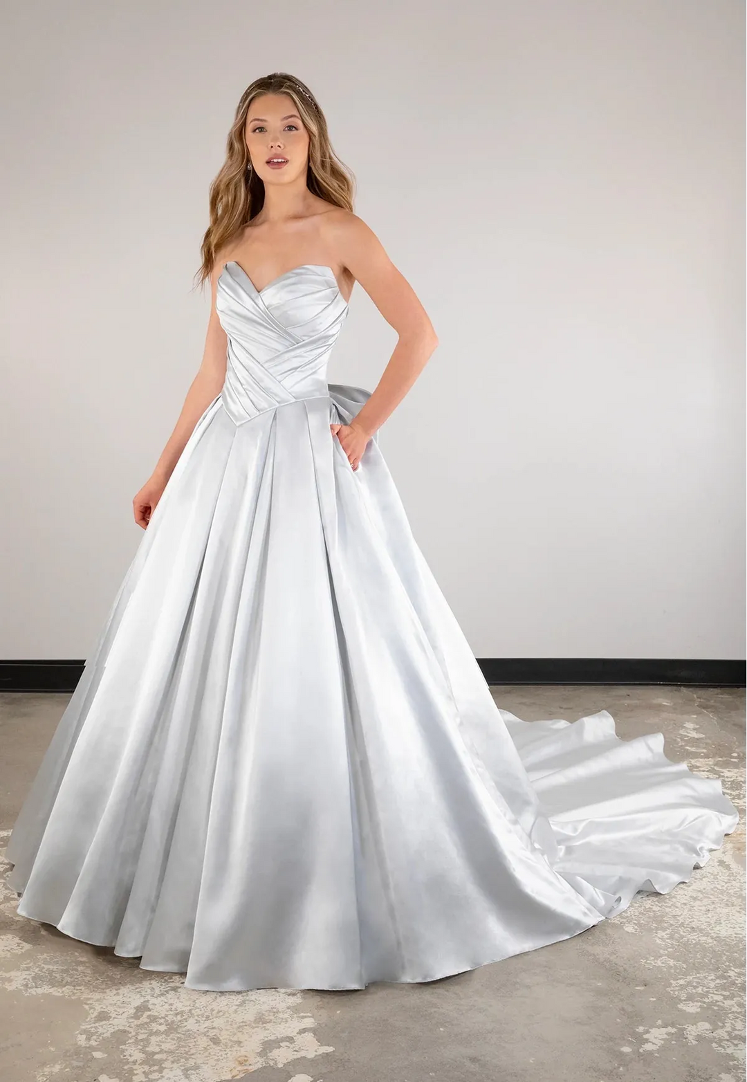 Woman wearing a strapless white wedding dress with a flowing skirt on a plain background