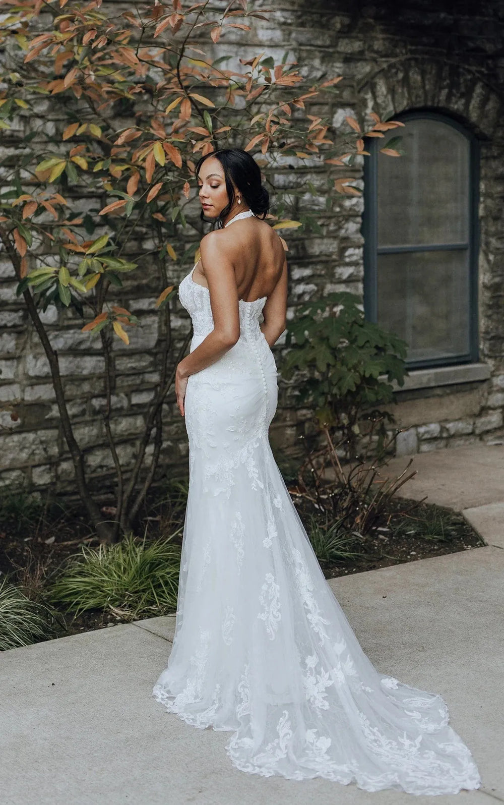 Woman in a white wedding dress standing against a stone wall with autumn leaves.