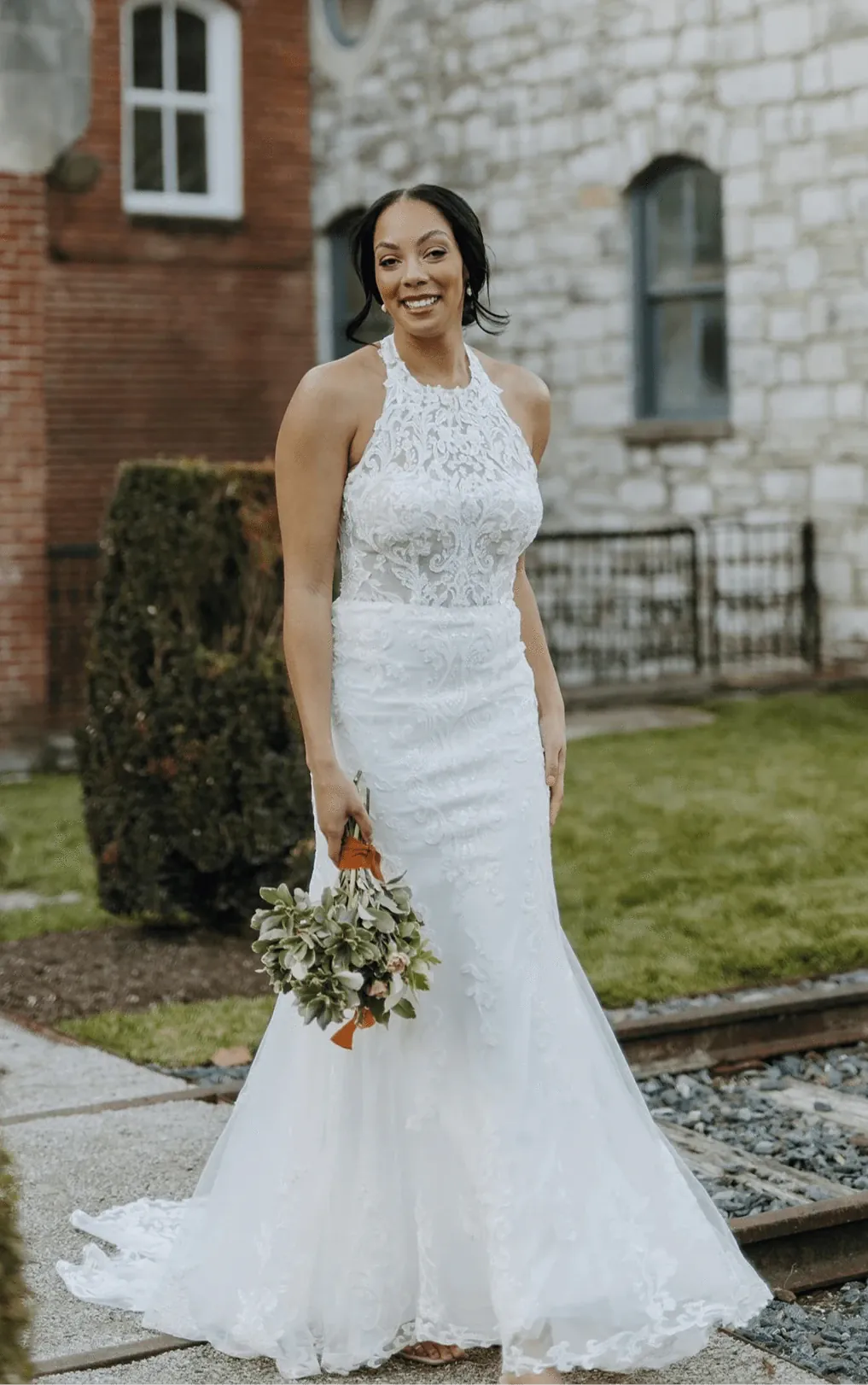 Woman in a white wedding dress holding a bouquet in front of a stone building.