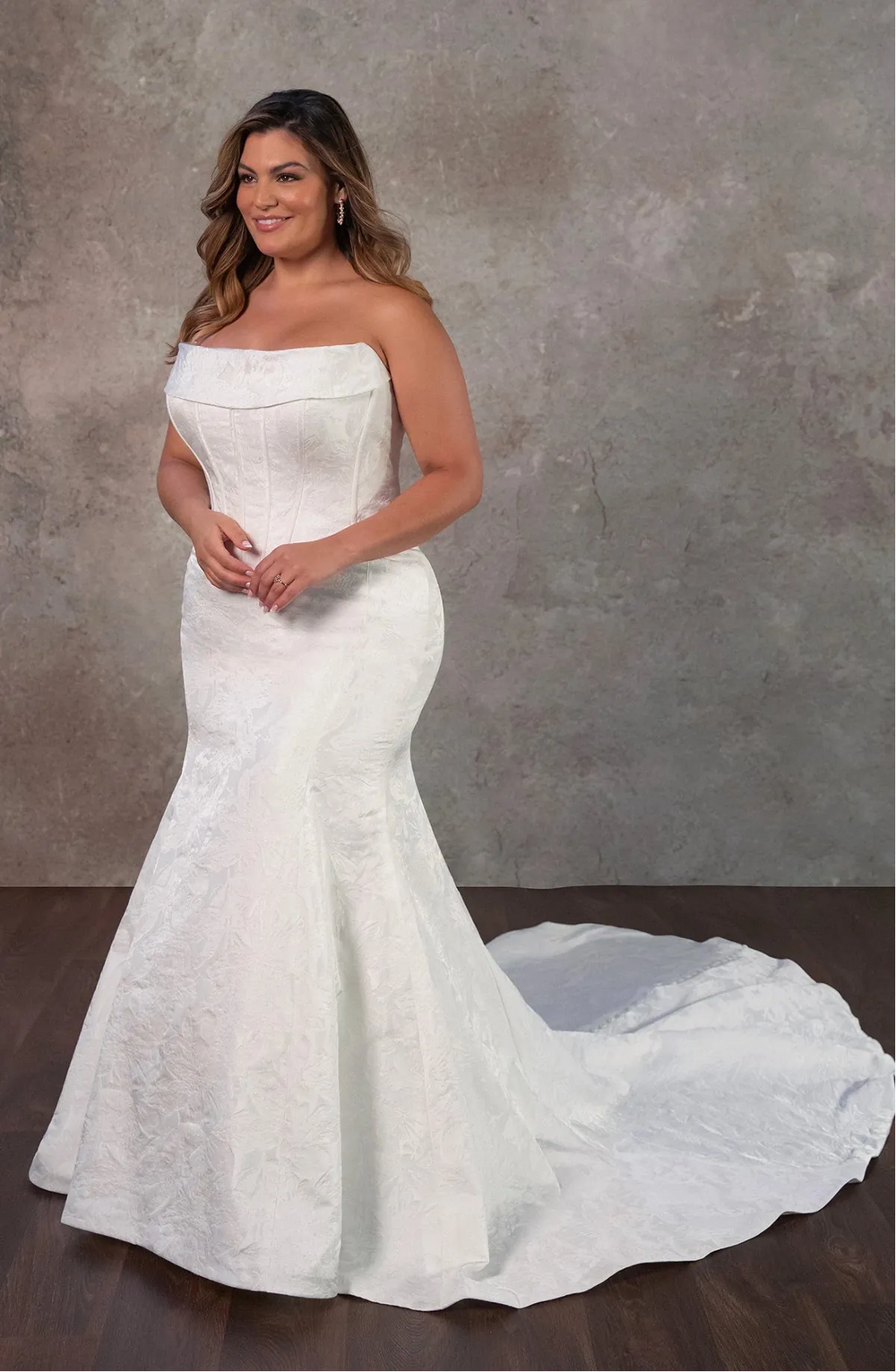 Woman wearing a white strapless wedding dress with a long train against a gray background