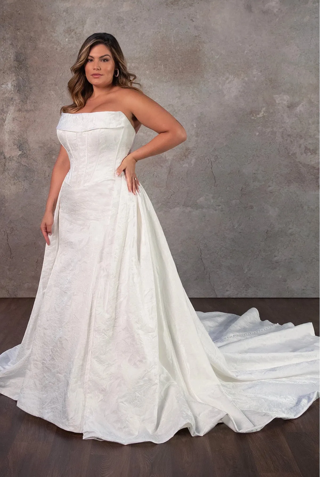 Woman wearing a strapless white wedding dress against a gray background