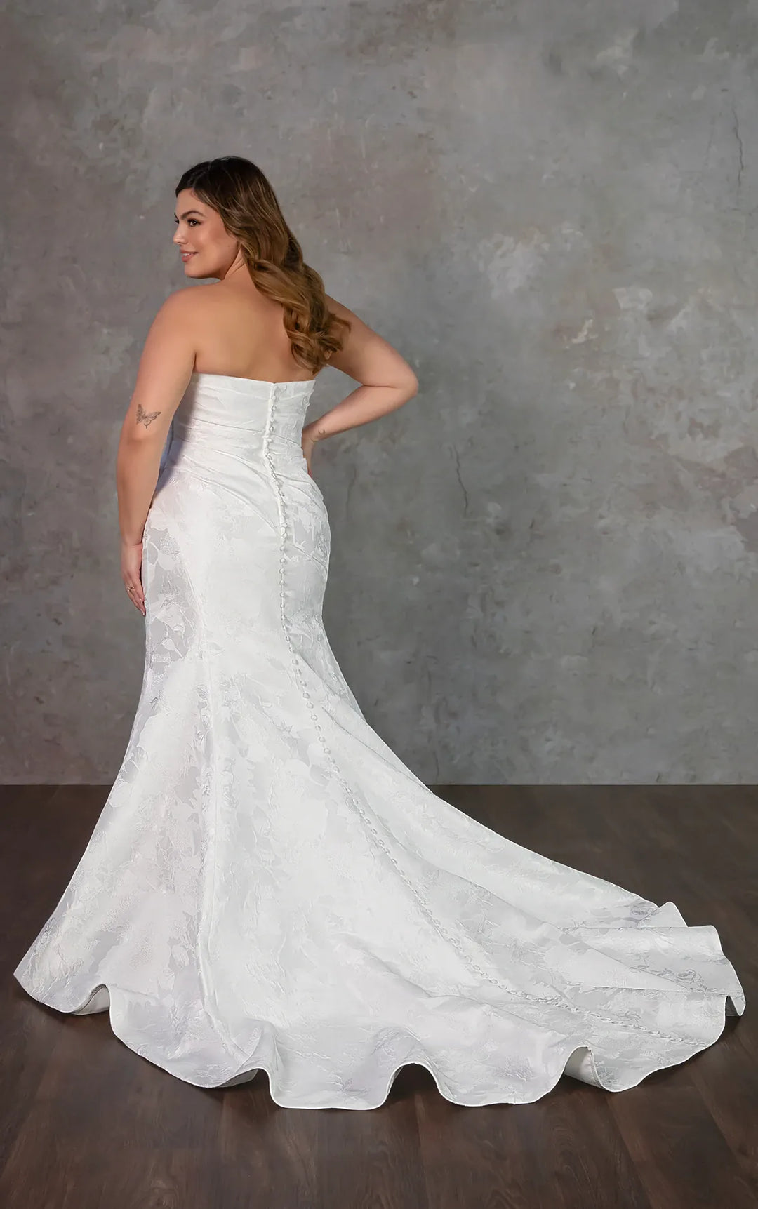 Woman wearing a strapless white wedding dress against a gray background