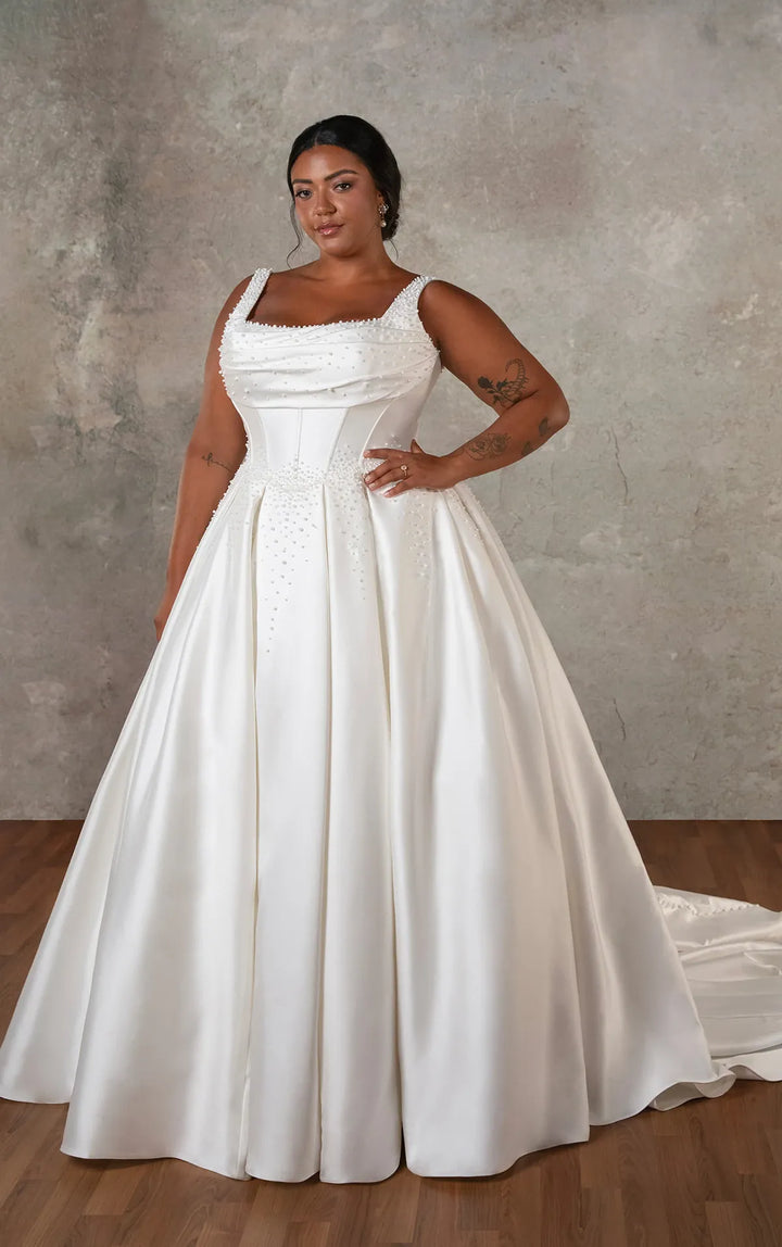 A woman modeling a white A-line wedding gown with a structured corset-style bodice, square neckline, and full satin skirt against a textured gray studio backdrop.
