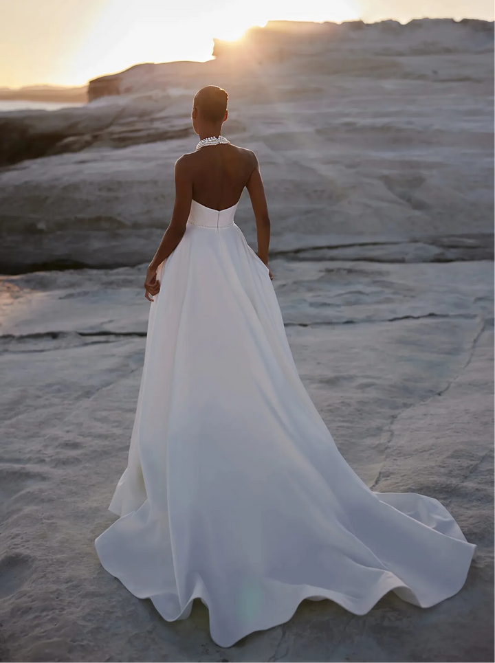 Woman in a white wedding dress standing on a rocky beach at sunset.