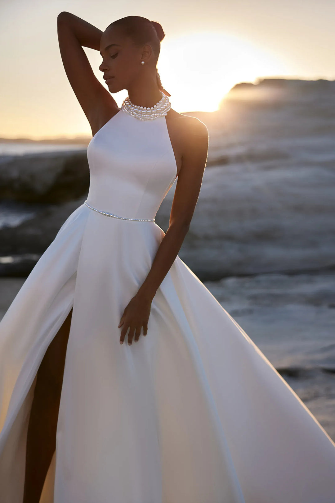 Woman in a white wedding dress standing on a beach with sunset in the background