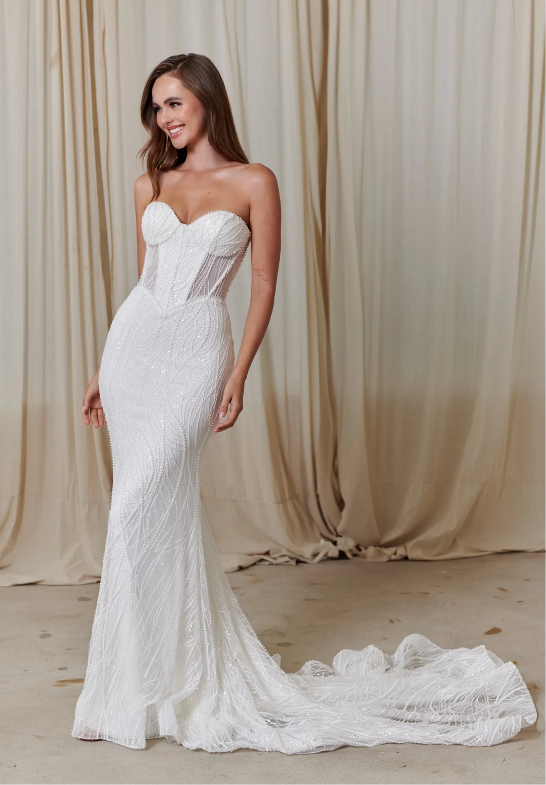 Woman wearing a white lace wedding dress against a beige curtain background