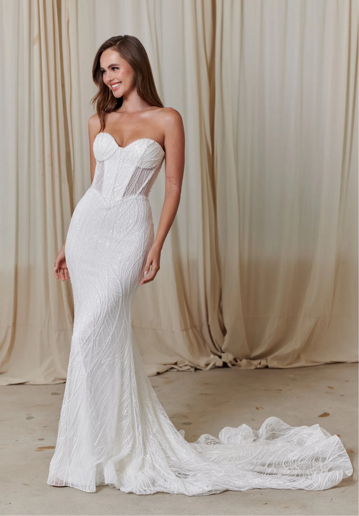 Woman wearing a white lace wedding dress against a beige curtain background