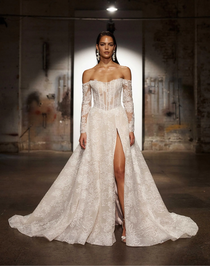front of evie young chevelle mocha lace a-line wedding dress showing the off the shoulder long sleeve neckline and thigh high slit in the skirt
