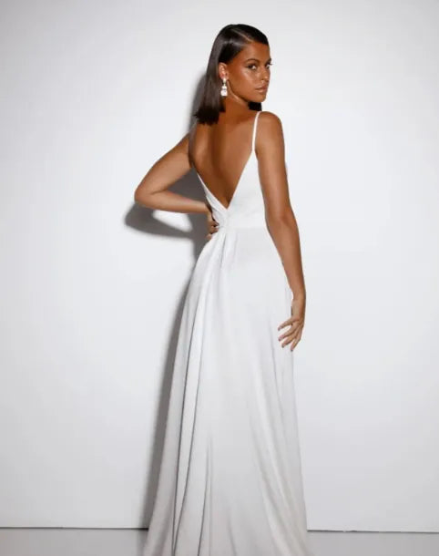 A woman modeling a white floor-length gown from the back, showing a deep V-back and gathered waist, against a plain white studio background.
