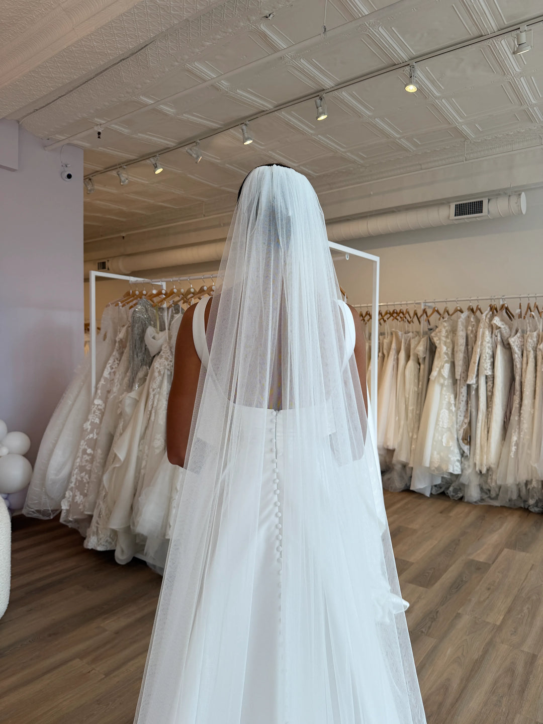 White wedding veil held by a person in a bridal gown showroom.