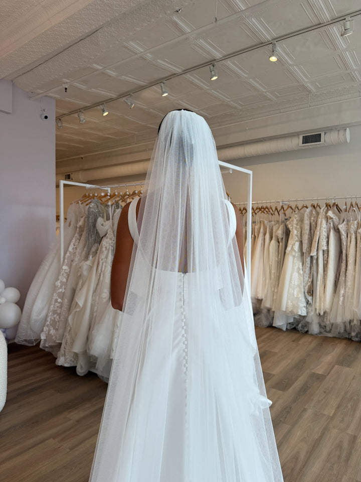 White wedding veil held by a person in a bridal gown showroom.