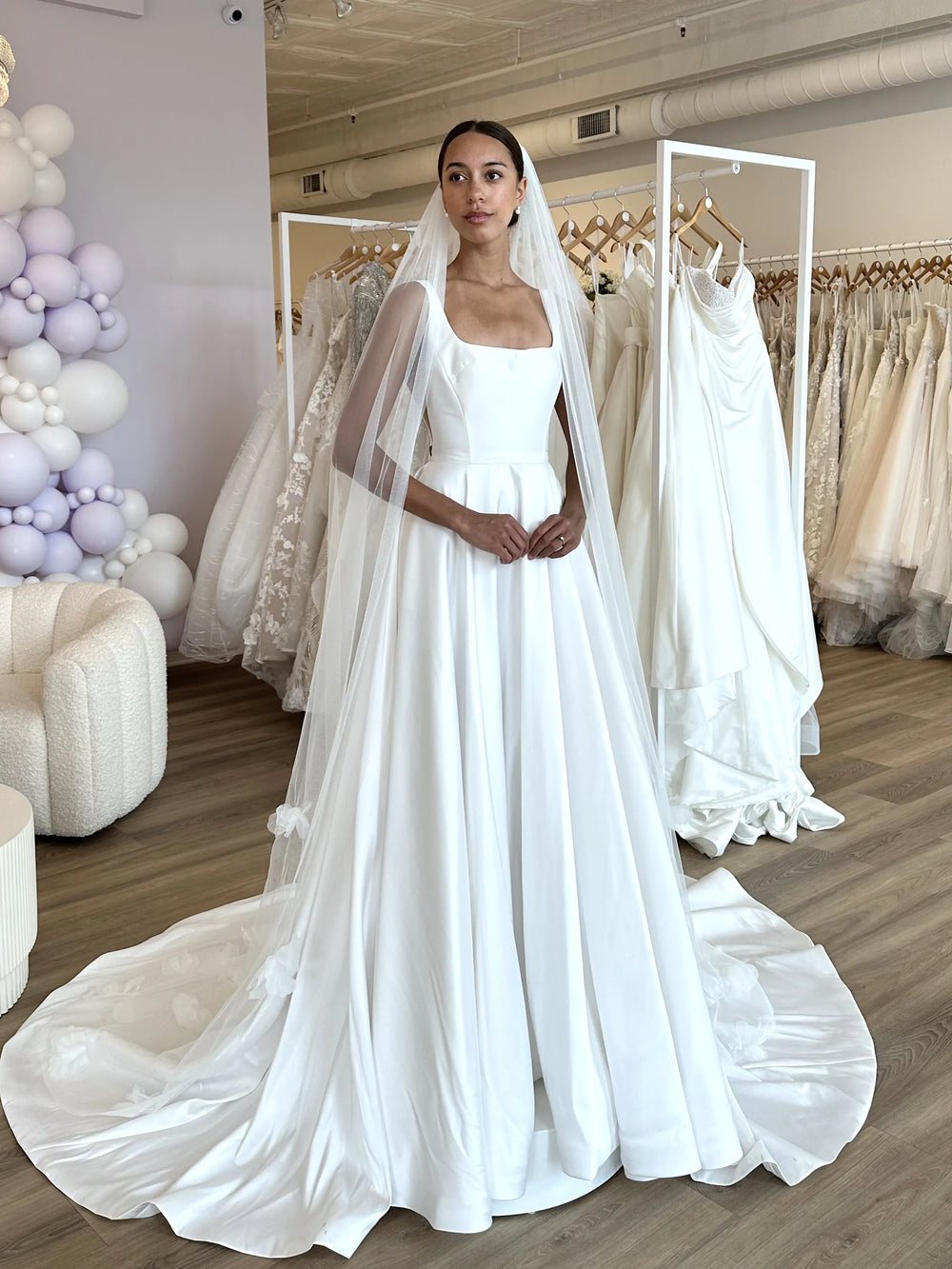Woman wearing a white wedding dress with a long train in a bridal shop.