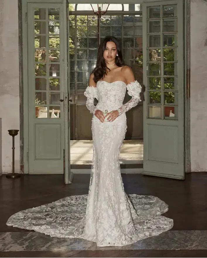 Woman in a white lace wedding dress standing in a room with large green doors.