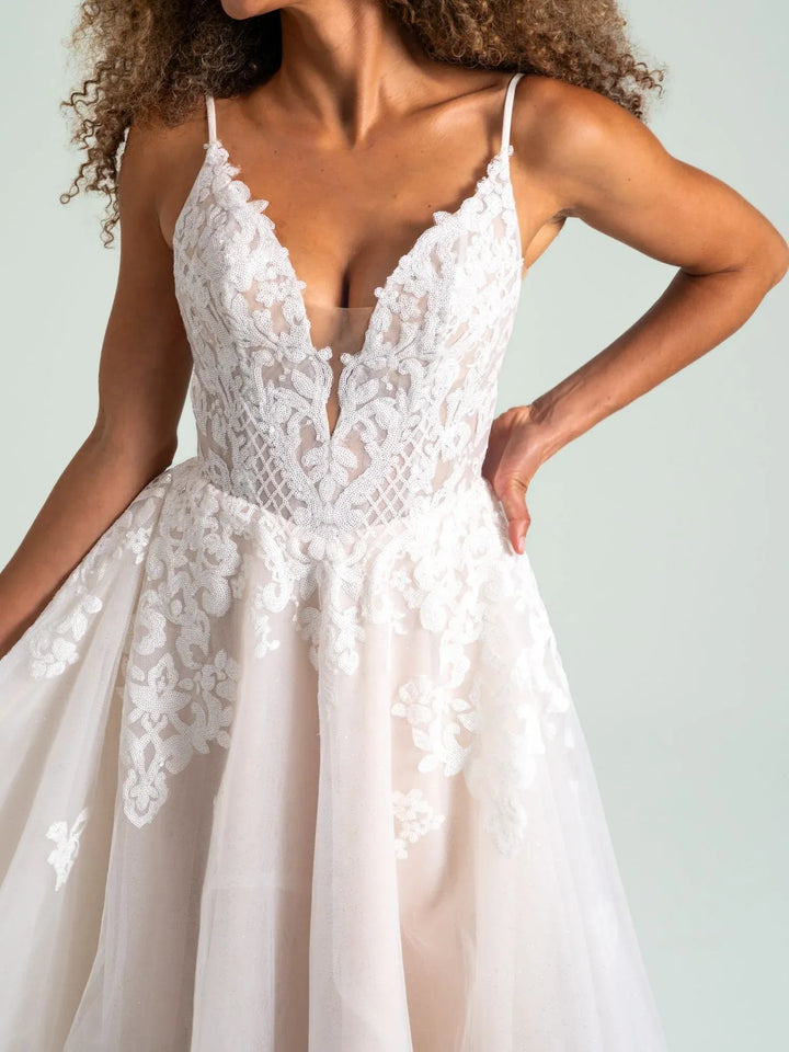 White lace and tulle A-line dress with thin spaghetti straps, a deep V-neckline, and a full skirt, shown on a model against a light gray background.