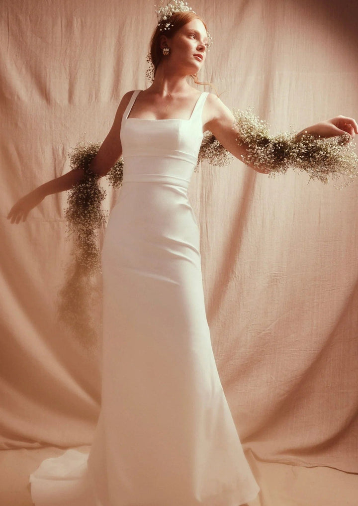 Woman in a white dress with embellished sleeves against a plain background