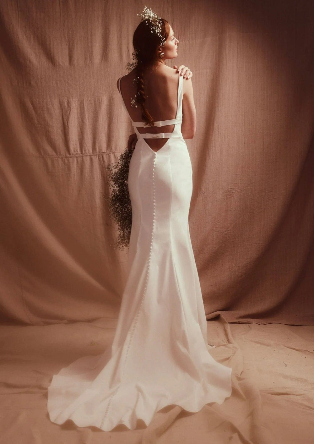 Woman in a white wedding dress with cut-out design standing against a brown backdrop