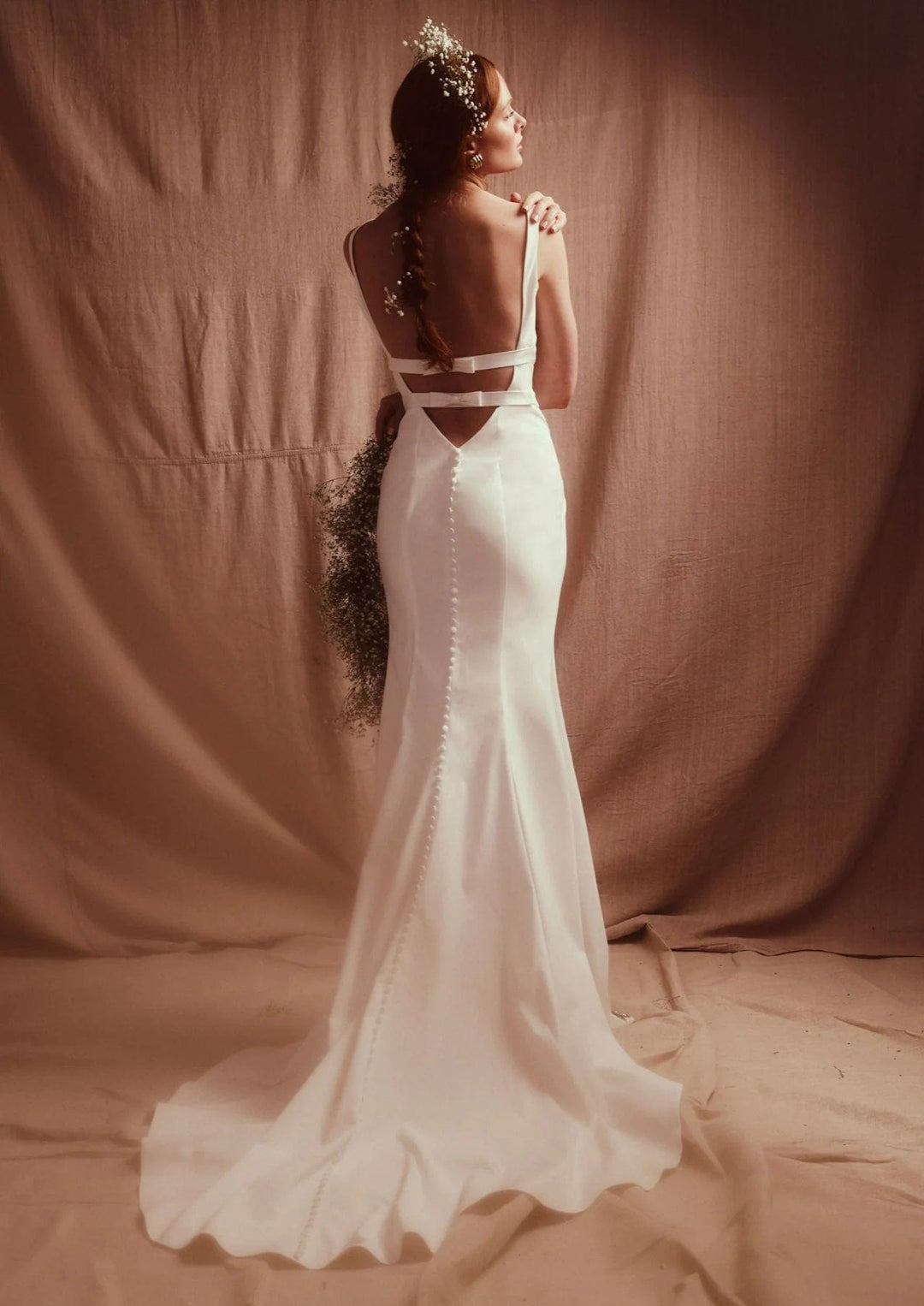 Woman in a white wedding dress with cut-out design standing against a brown backdrop