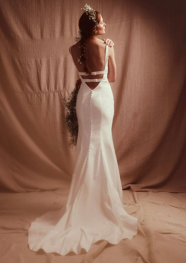 Woman in a white wedding dress with cut-out design standing against a brown backdrop