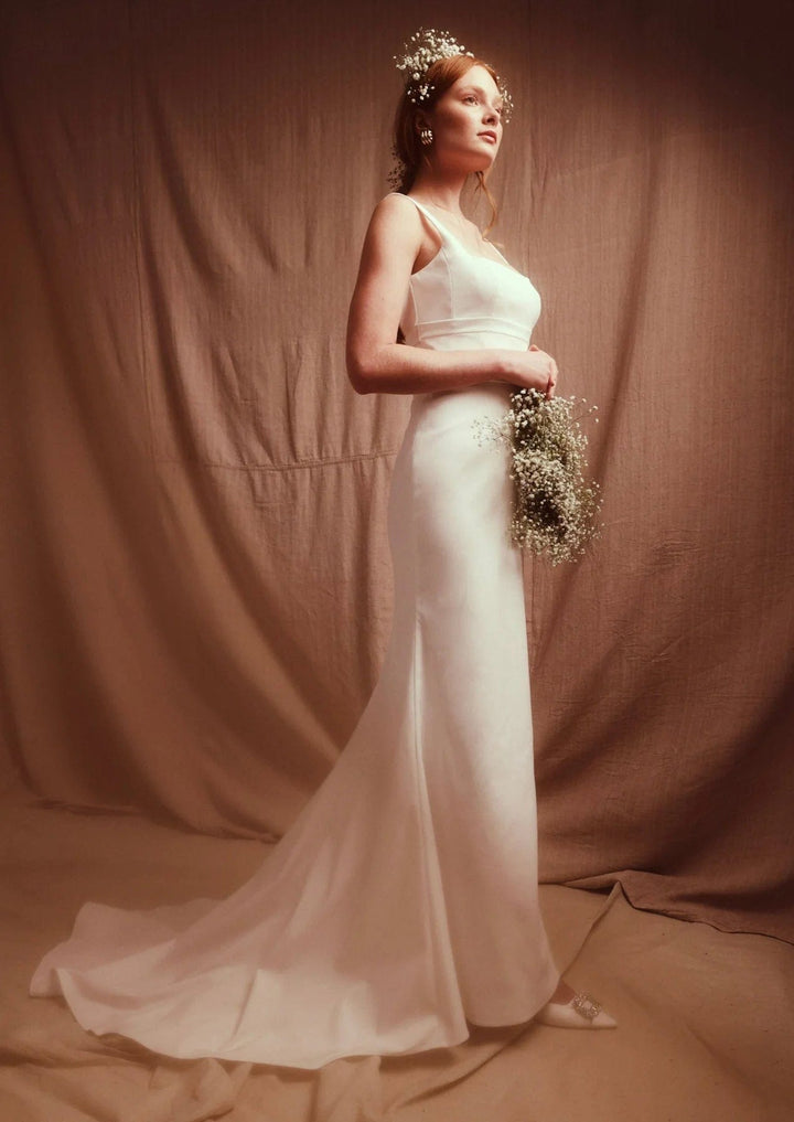 Bride in a white wedding dress holding a bouquet against a brown backdrop