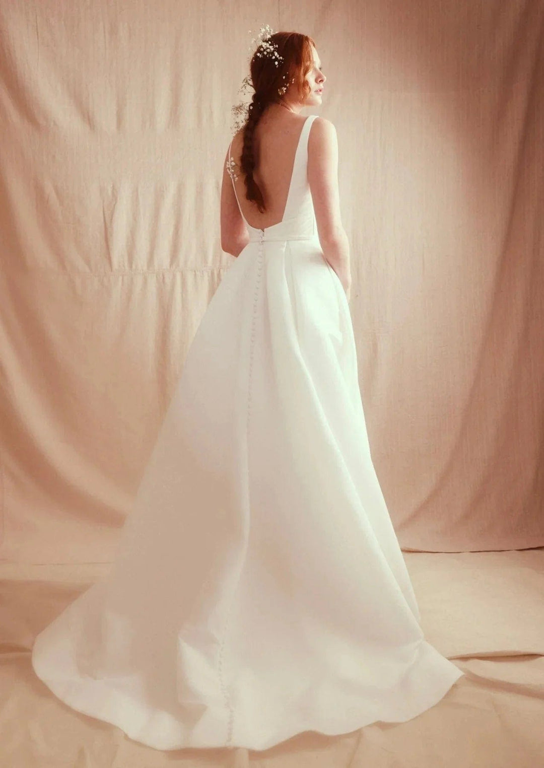 Woman in a white wedding dress standing against a plain background