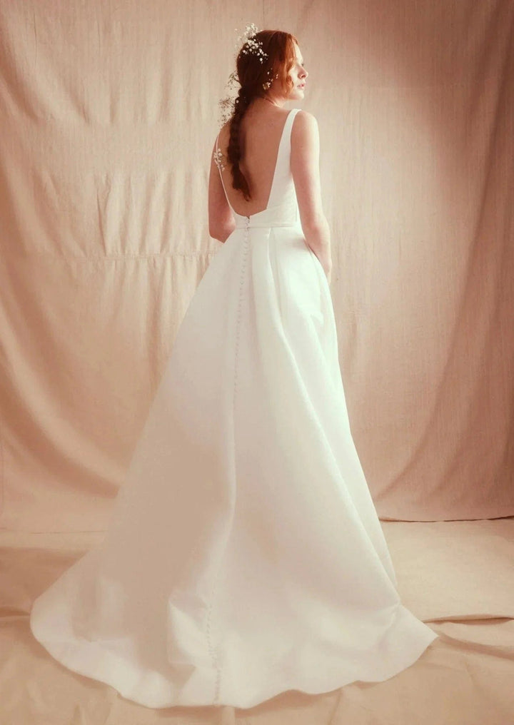 Woman in a white wedding dress standing against a plain background