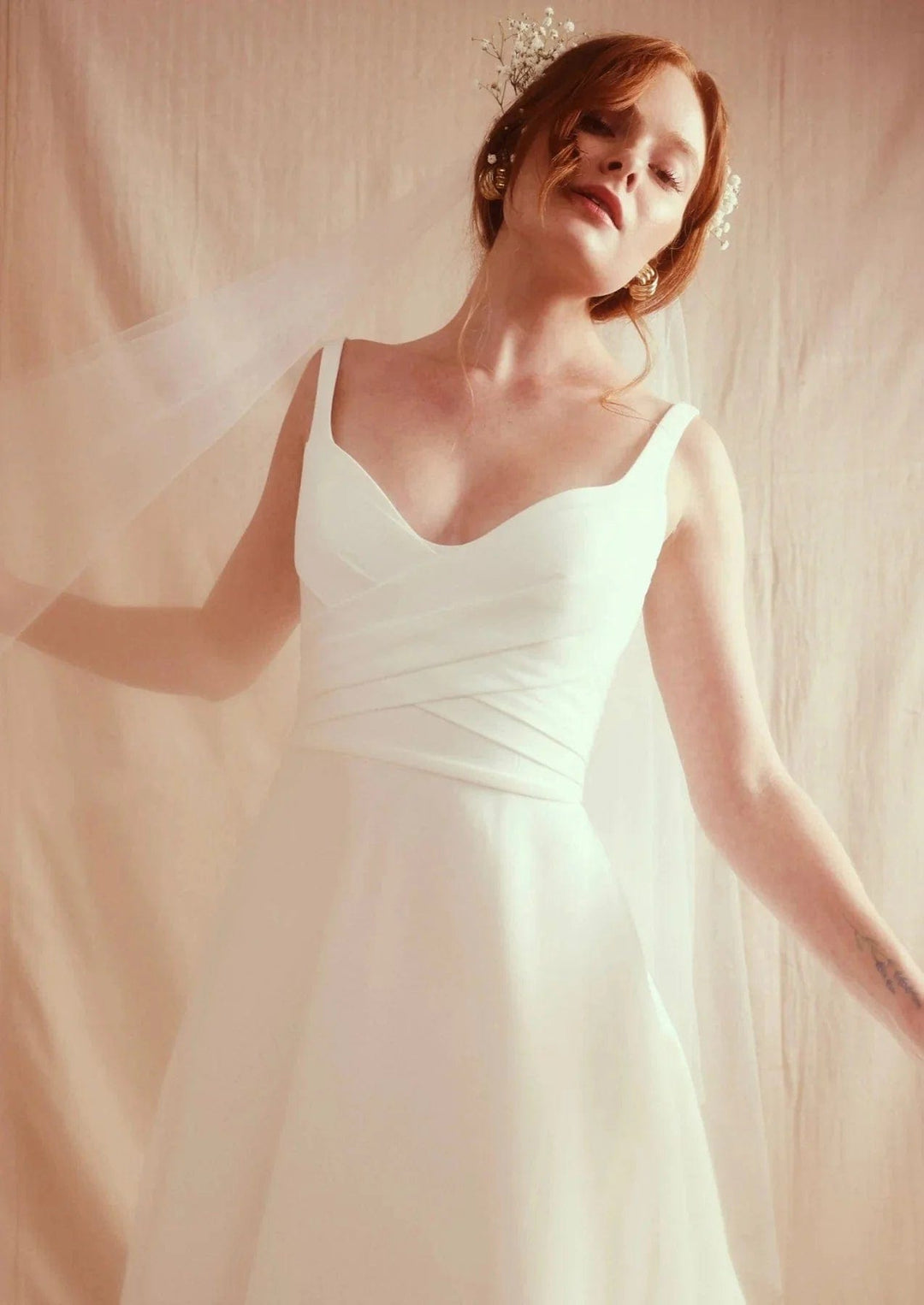 Woman in a white dress standing against a soft, neutral background