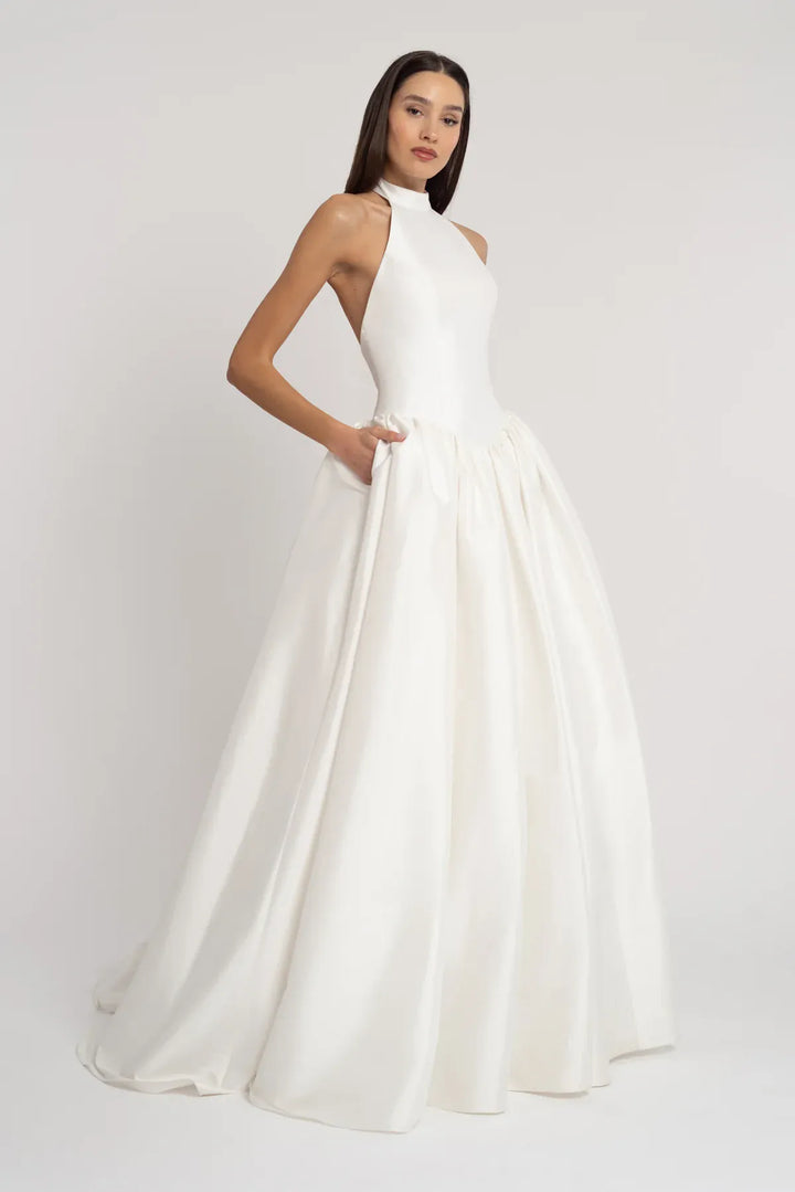 Woman wearing a white halter neck gown on a plain background