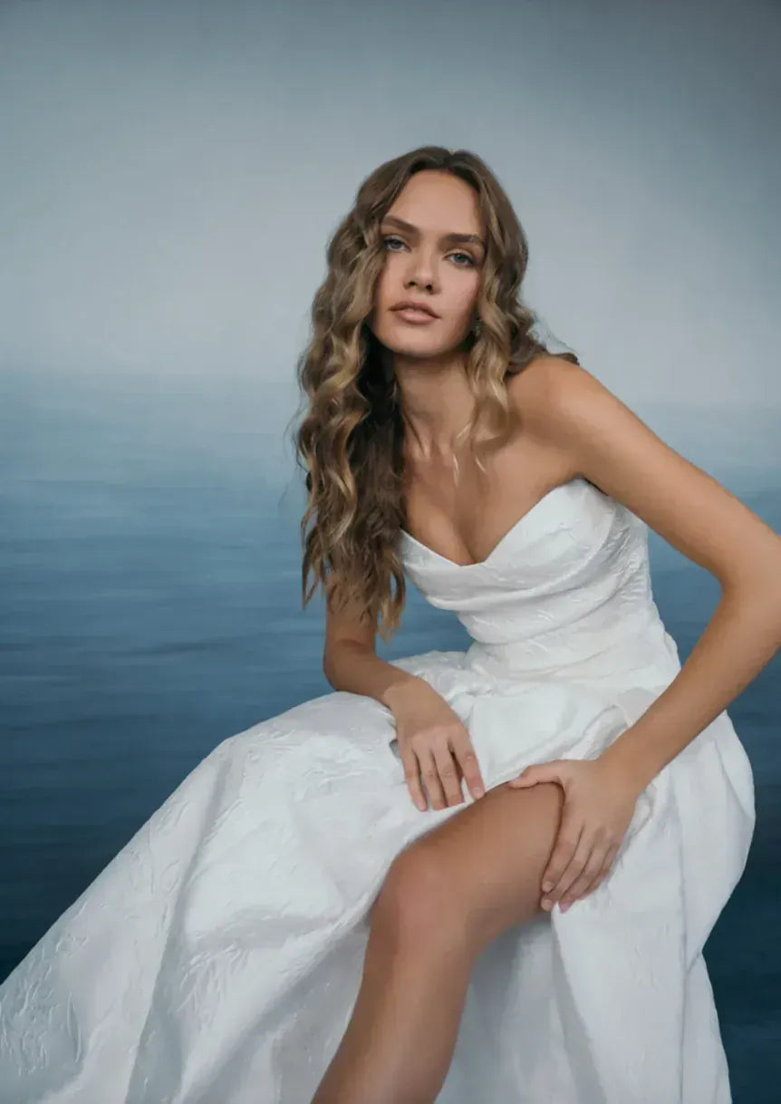 Woman in a white wedding dress sitting by the water with a blurred background