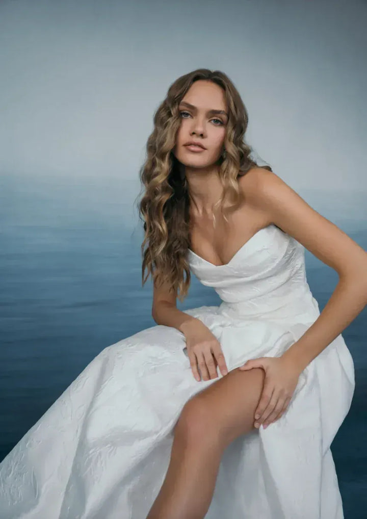 Woman in a white wedding dress sitting by the water with a blurred background
