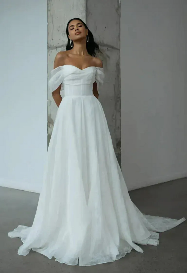 Woman wearing a white off-shoulder wedding dress against a plain background