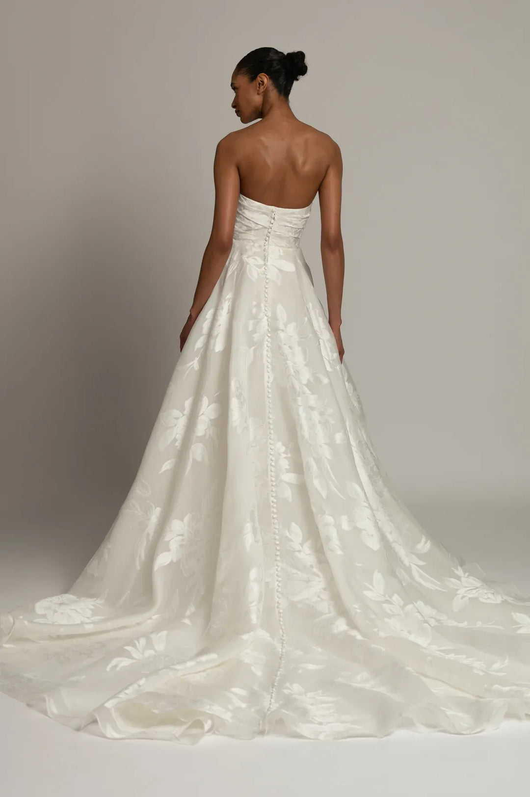 A strapless white wedding gown with a structured bodice and a full, flowing skirt, shown from the back on a model against a neutral studio background.