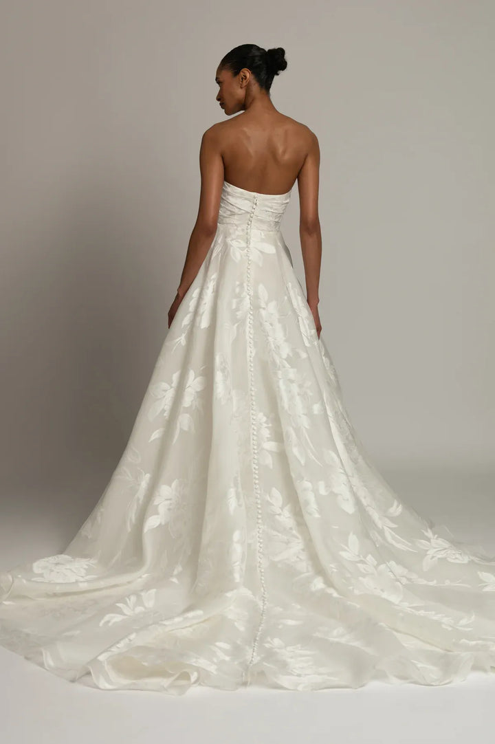 A strapless white wedding gown with a structured bodice and a full, flowing skirt, shown from the back on a model against a neutral studio background.
