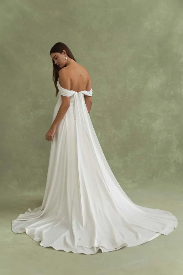 Woman wearing a white wedding dress with a long train on a green background