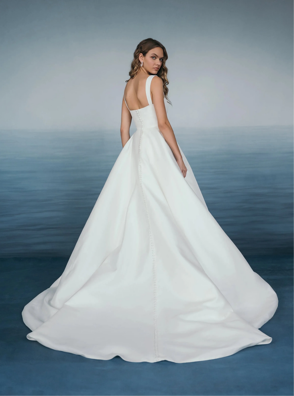 Woman in a white wedding dress standing against a blue water background