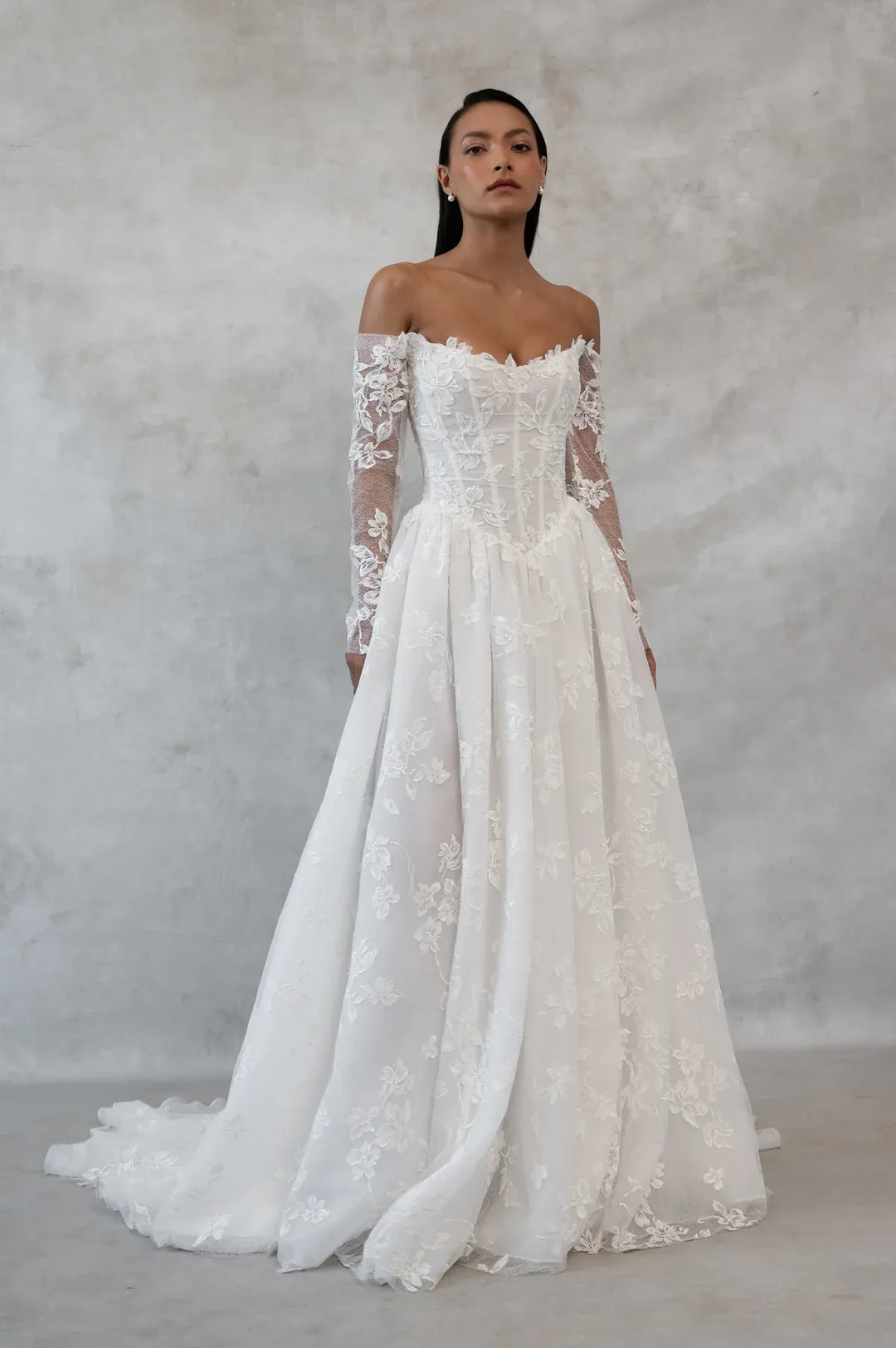 Woman wearing a white lace wedding dress against a plain background