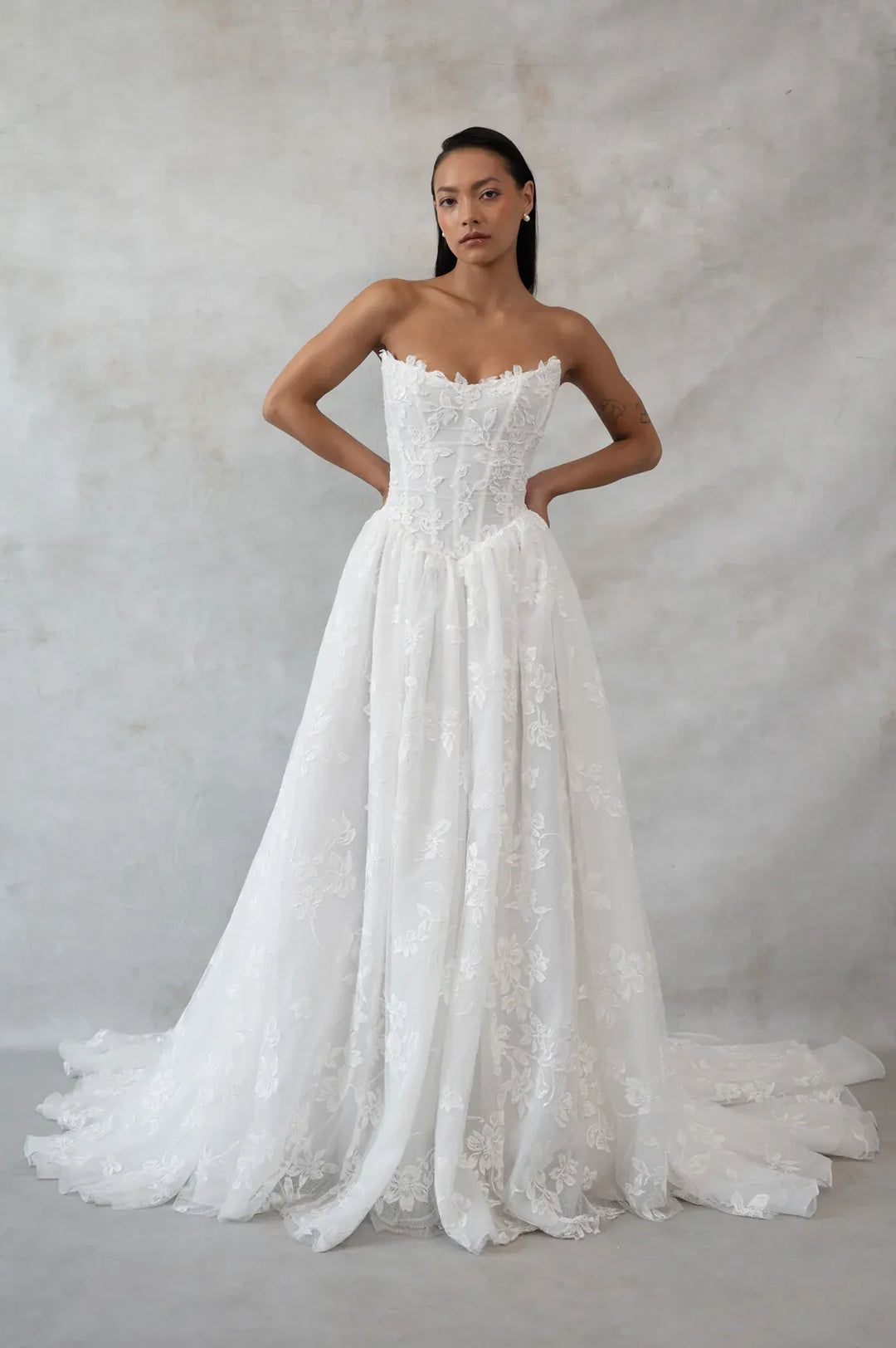 Woman wearing a strapless lace wedding dress against a plain background