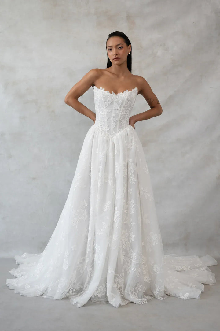 Woman wearing a strapless lace wedding dress against a plain background