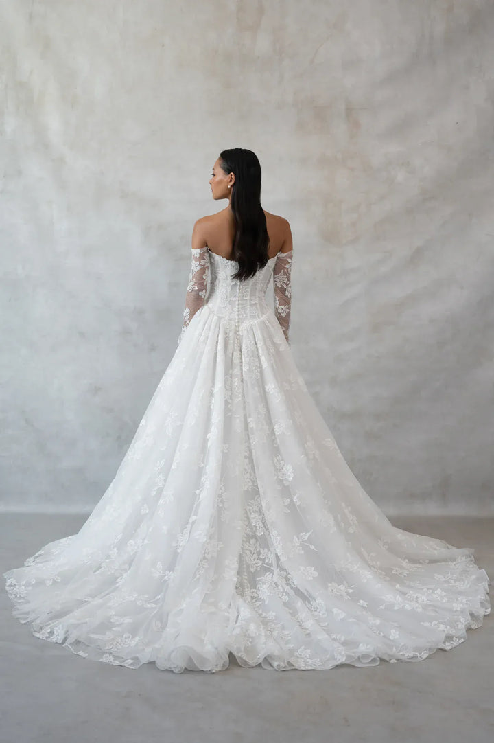 Woman wearing a white lace wedding dress against a plain background