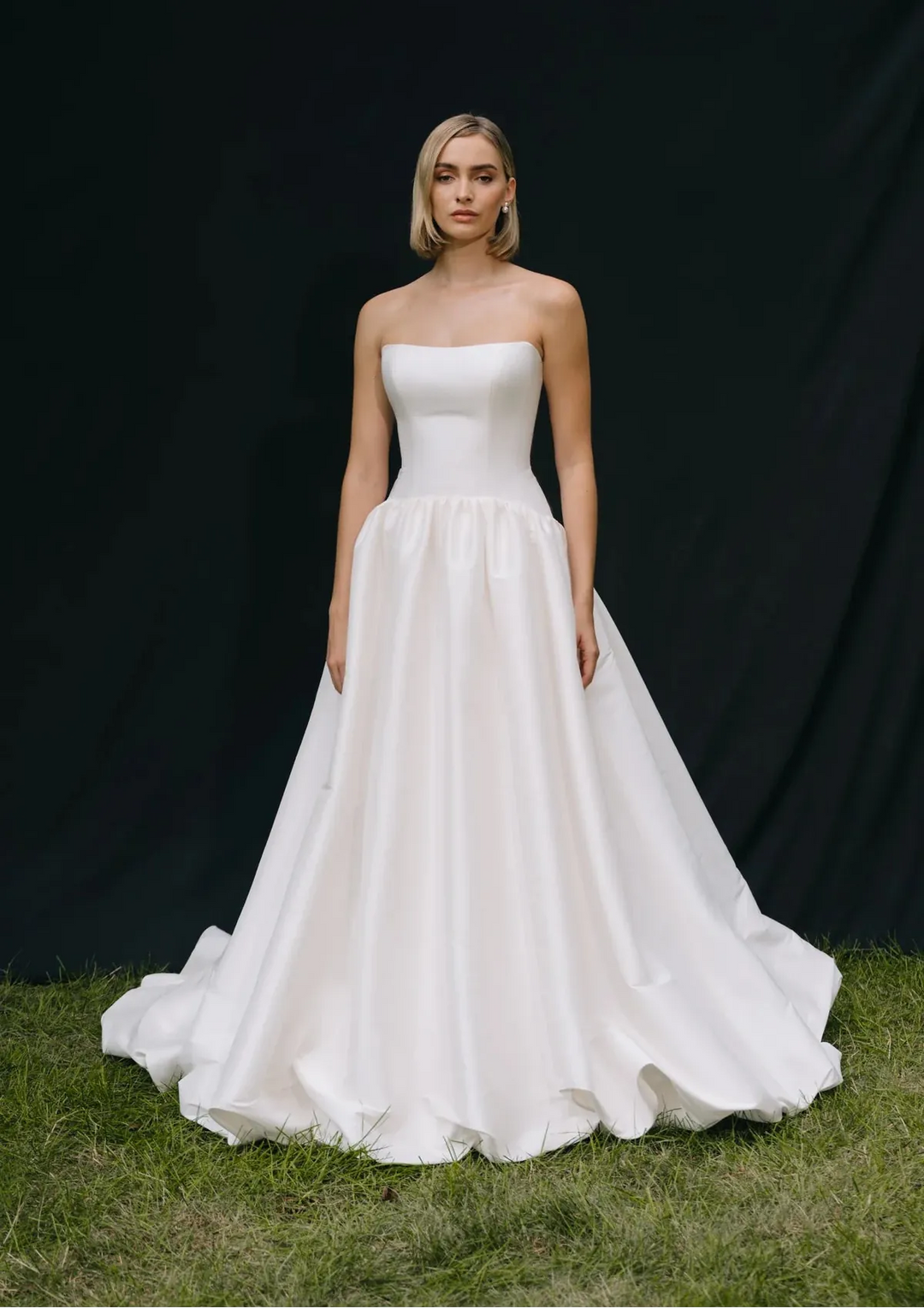 Woman wearing a strapless white wedding dress against a black background