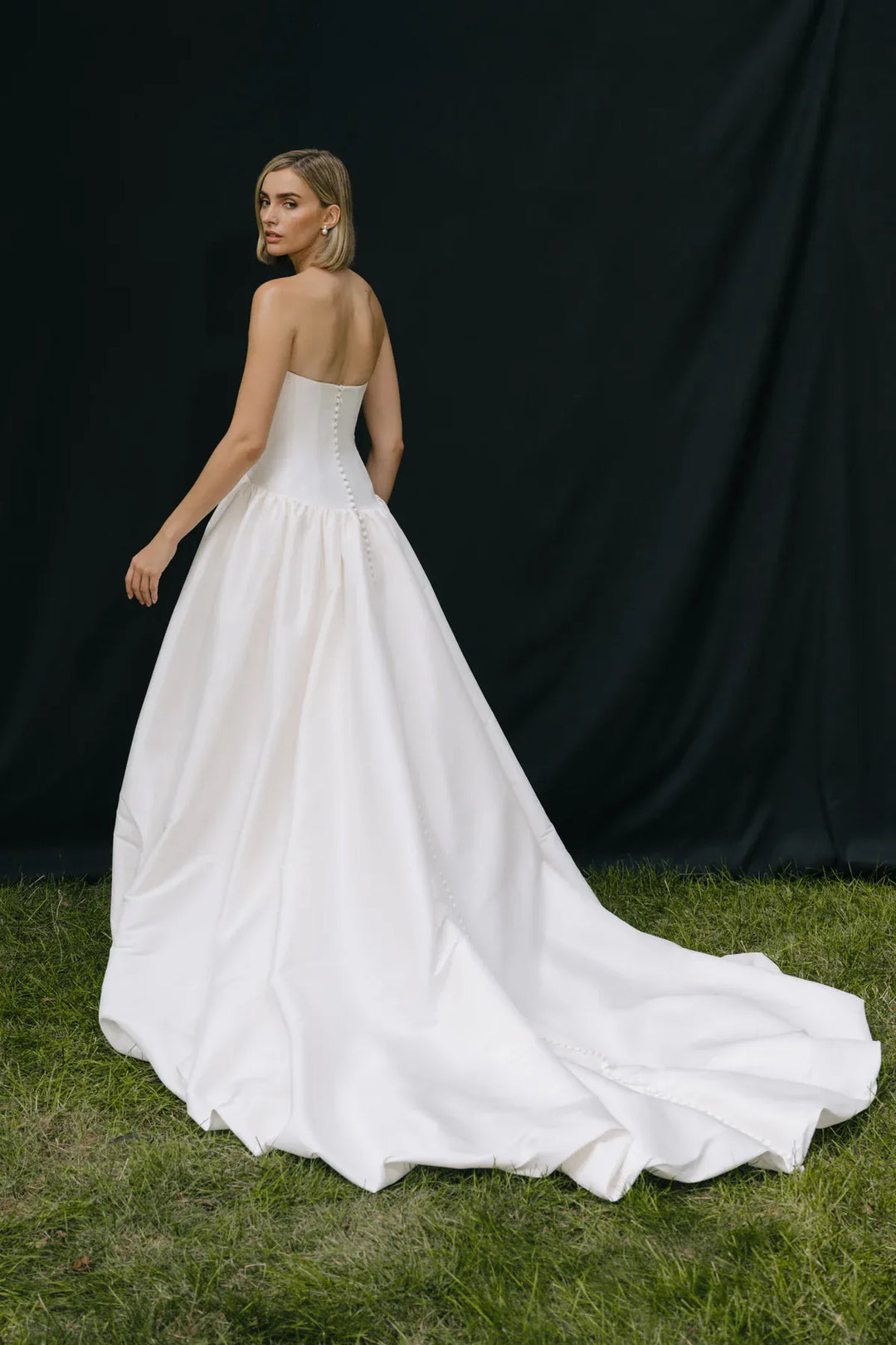 Woman in a white wedding dress standing on grass with a black backdrop