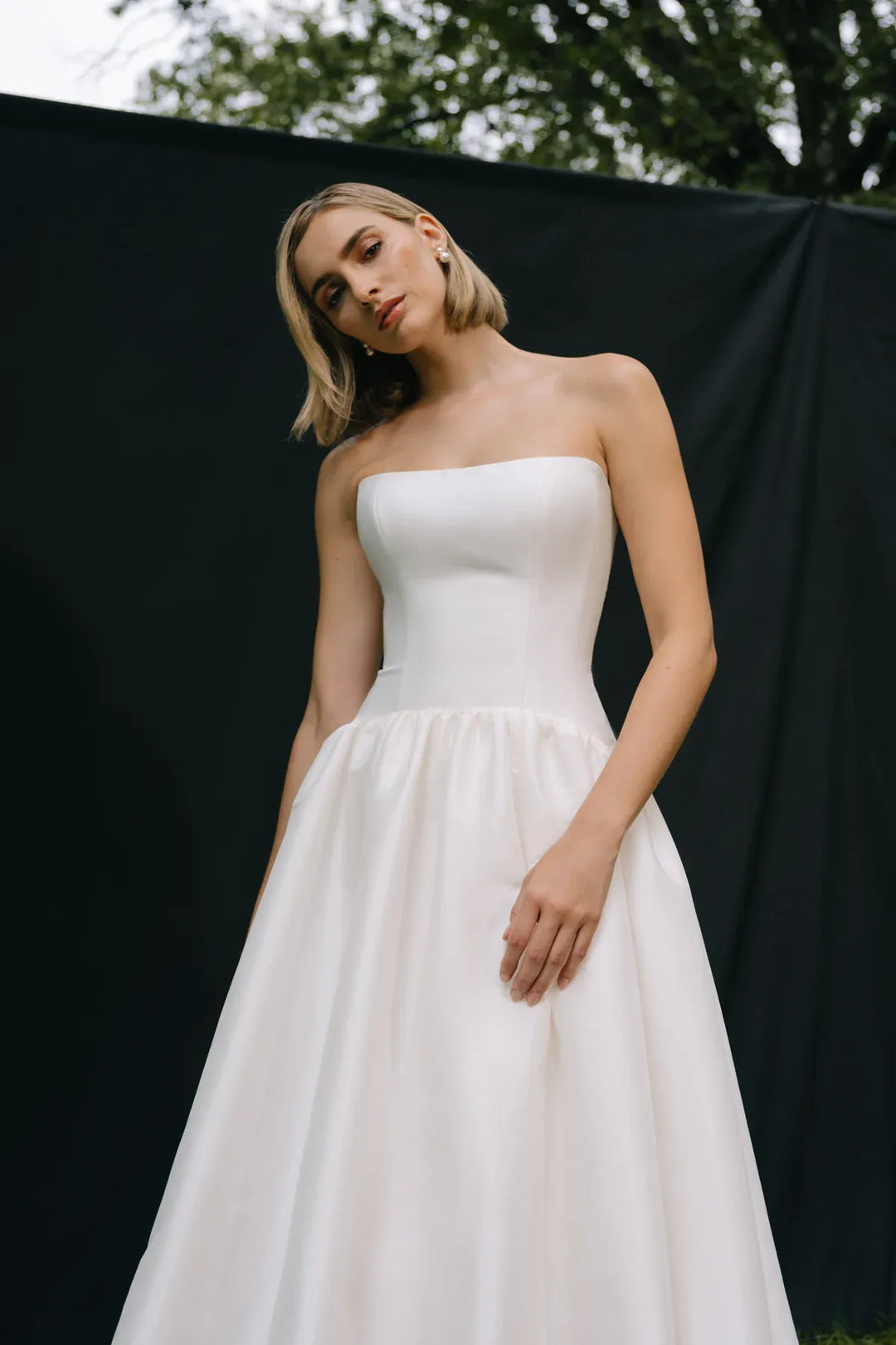 Woman wearing a strapless white wedding dress against a black backdrop